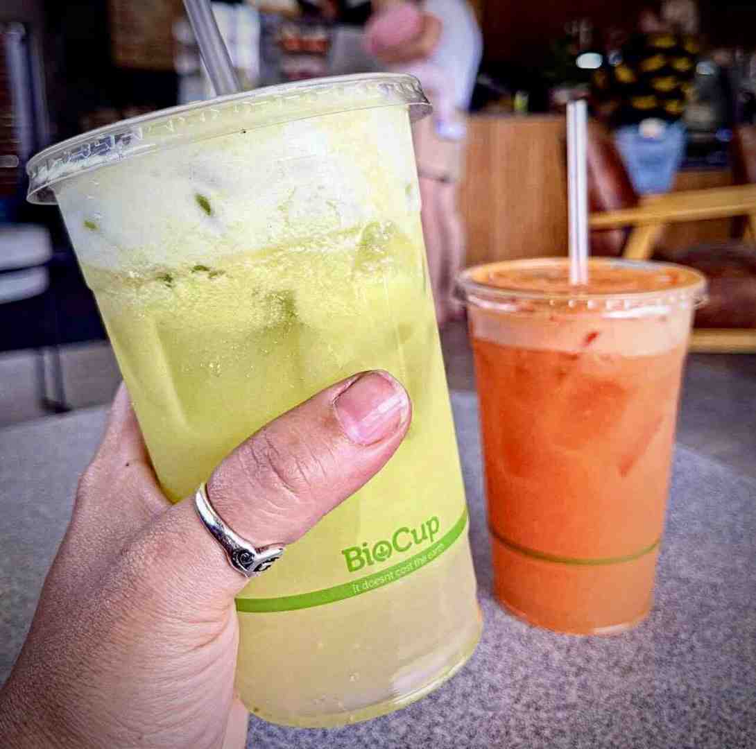 Hand holding a large, green iced drink in a sustainable BioCup alongside an ice fruit drink. These quality cold drinks are great summer drinks to order. Hand holding a large, green iced drink in a sustainable BioCup alongside an ice fruit drink. These quality cold drinks are great summer drinks to order.