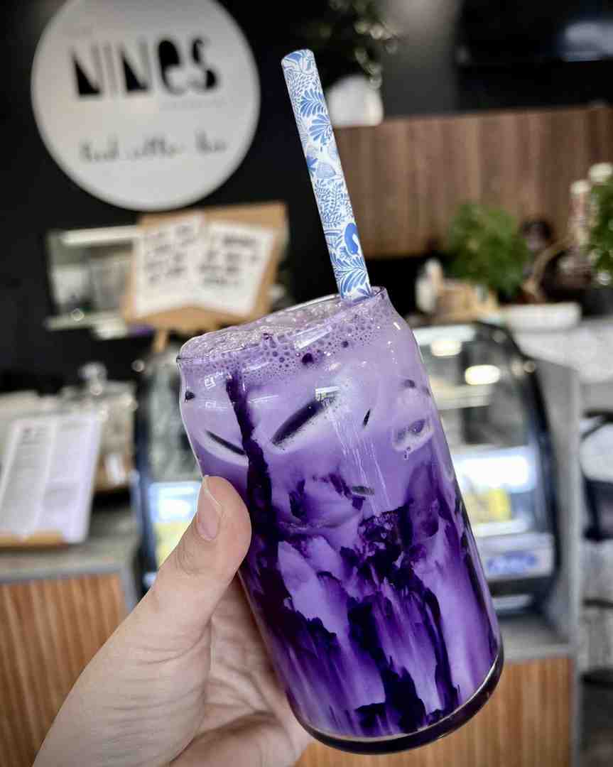 A vibrant, unique iced Ube Taro latte with swirling purple colouration and a patterned straw, served in a can-shaped glass. This unique drink confirms the Sunshine Coast best coffee status.