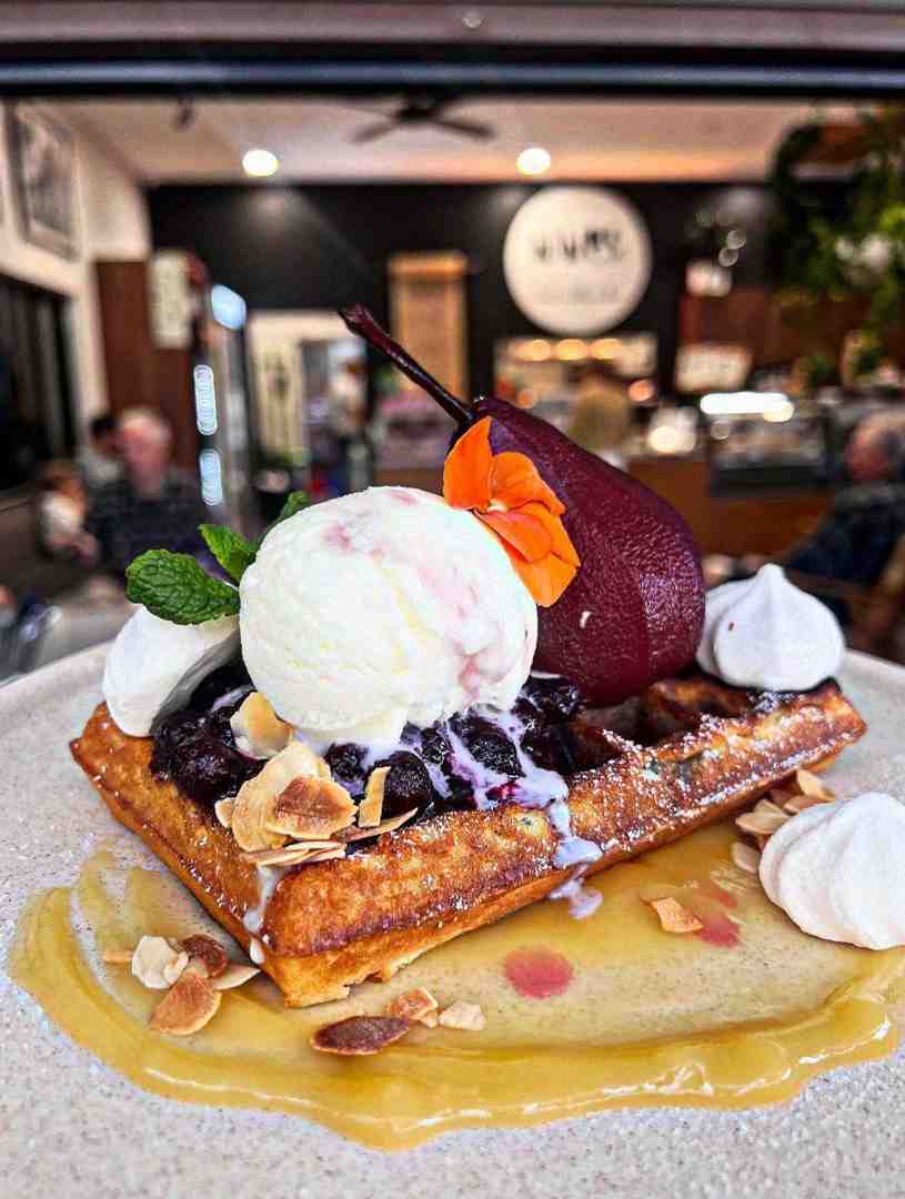 A Belgian waffle topped with a blueberry poached pear, vanilla ice cream, and berry reduction, offering a sophisticated alternative to simple pancakes or waffles.