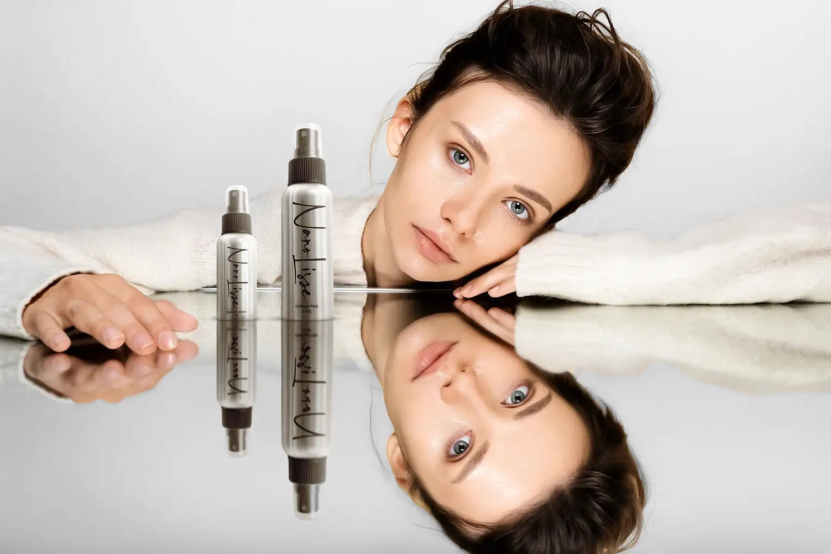 Model showcasing beauty hyaluronic acid facial mist bottles reflected on glass for glowing hydrated skin.