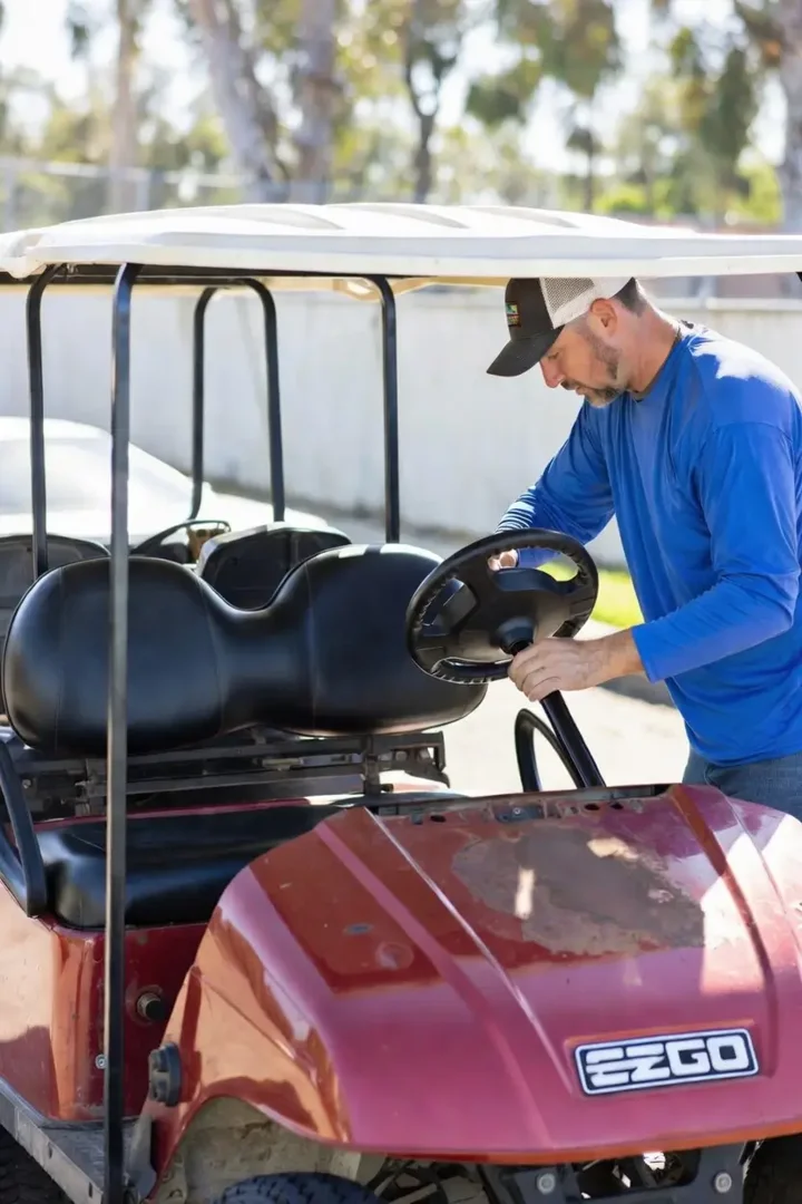 A mechanic in a well-lit shop identifying the serial number on an EZGO TXT frame - golf cart body kits for ezgo A mechanic in a well-lit shop identifying the serial number on an EZGO TXT frame - golf cart body kits for ezgo