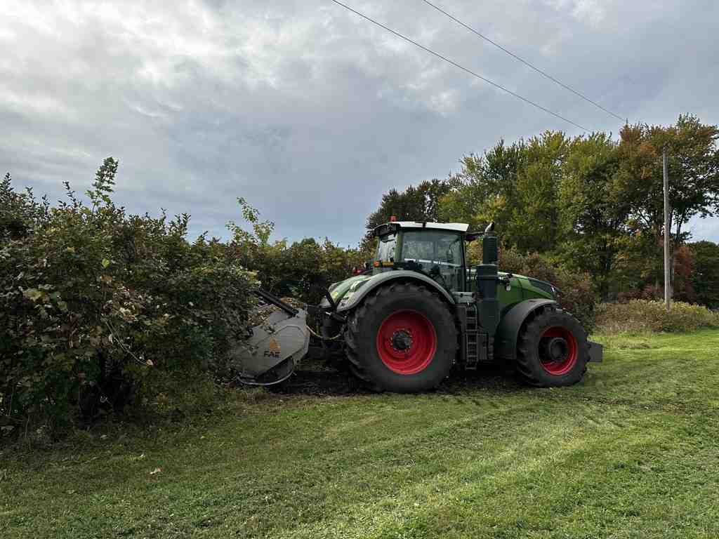 user-inserted Tractor performing forestry mulching in a field, demonstrating land clearing services.