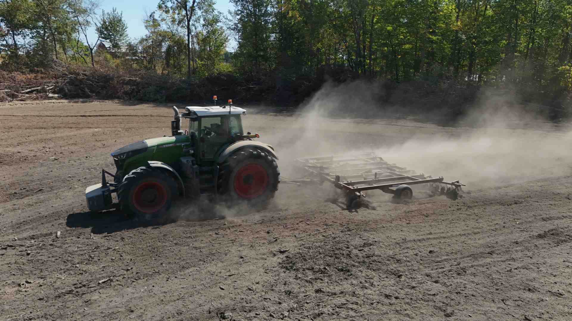 A powerful tractor attached to a large disc plow, actively tilling a field with rich, dark soil - plow disc