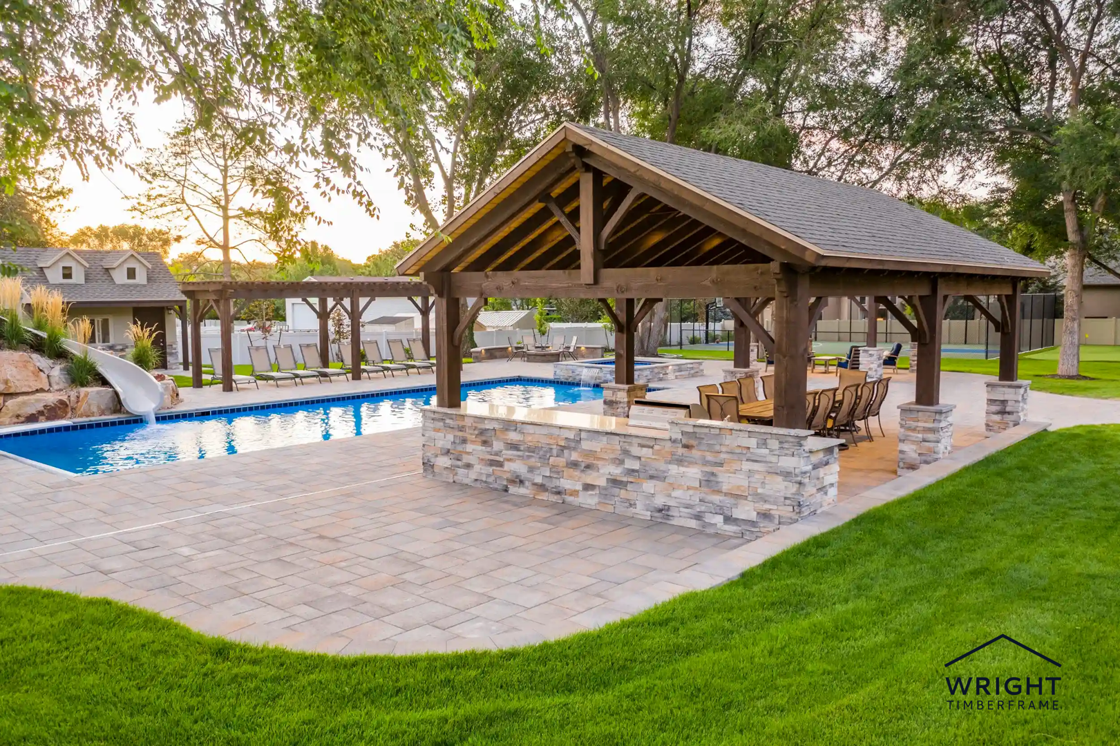 Custom outdoor pavilions built with timber framing beside a landscaped pool, featuring covered seating, stone accents, and open-air design