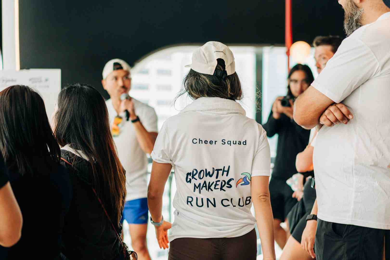 A person wearing a white t-shirt with “Cheer Squad” printed at the top and “Growth Makers Run Club” in bold, colorful letters on the back.