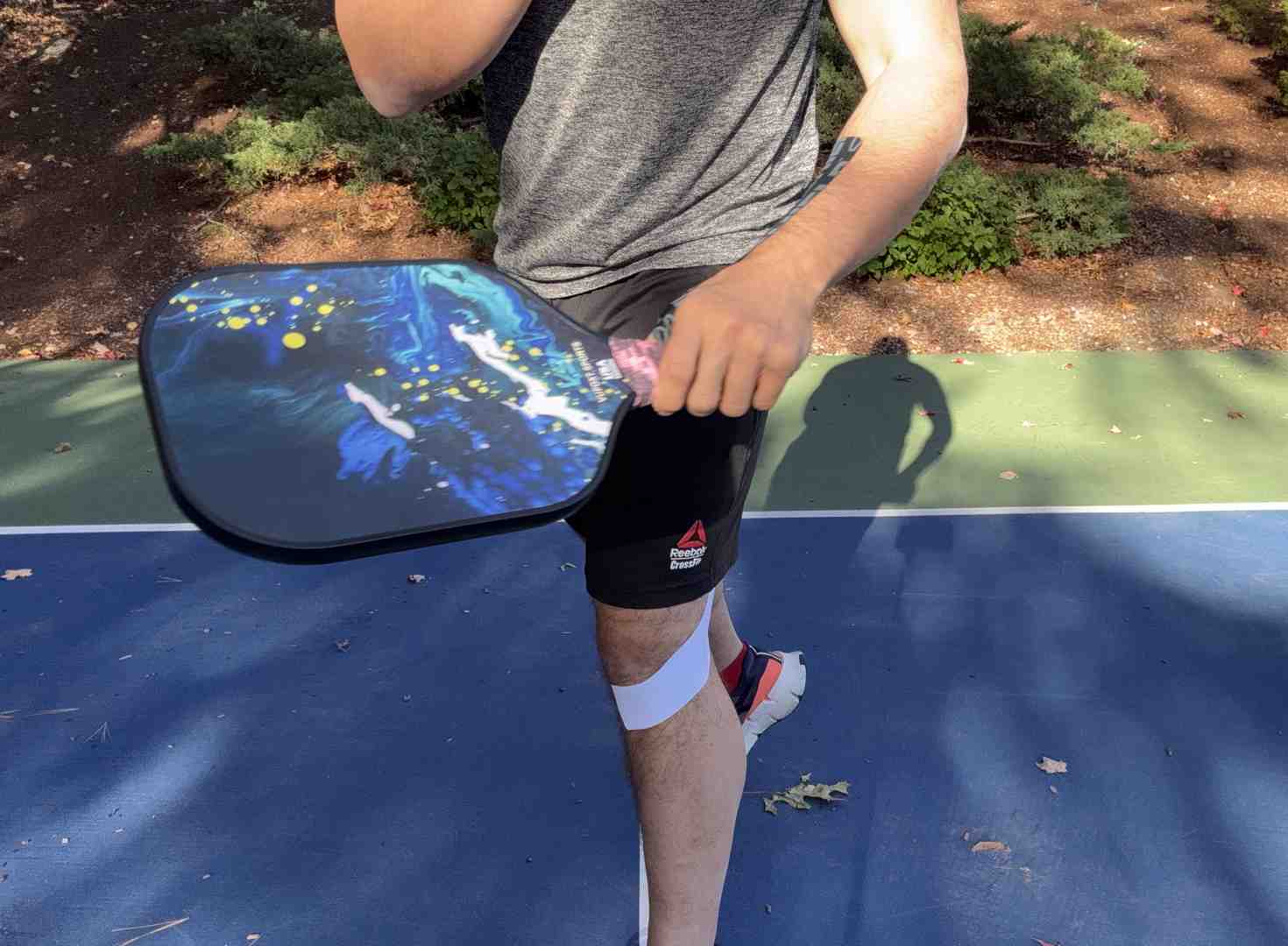 Photograph of a pickleball athlete poised to return, wearing Kinesiology pain around the knee and patella