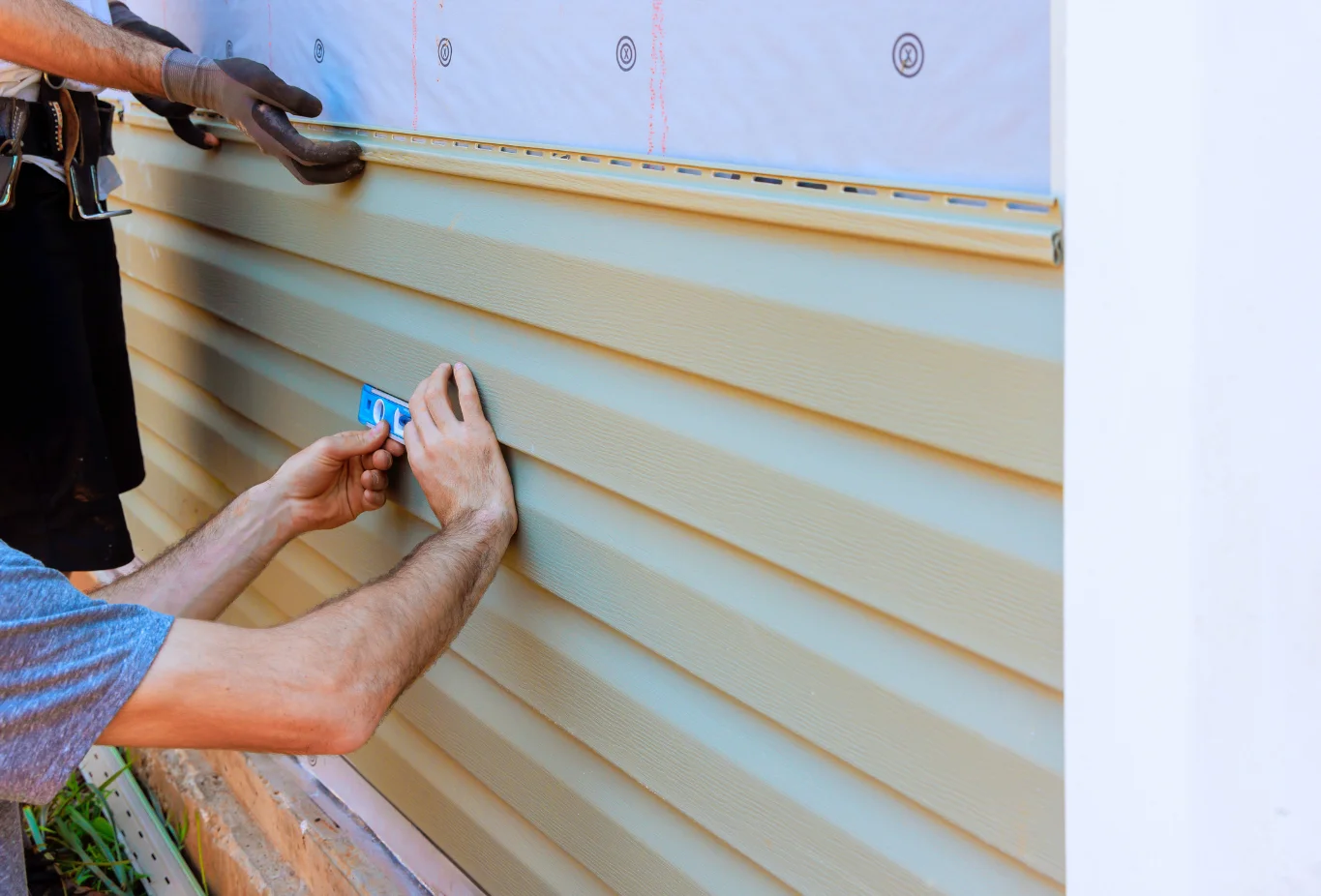 Contractor leveling beige vinyl siding panels during proper siding installation
