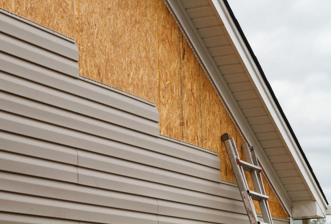 Vinyl siding replacement in progress with exposed OSB sheathing and beige siding on a residential home