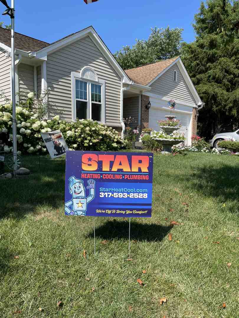 A STAR Heating Cooling Plumbing yard sign outside of a brick home with flowers in the yard. 