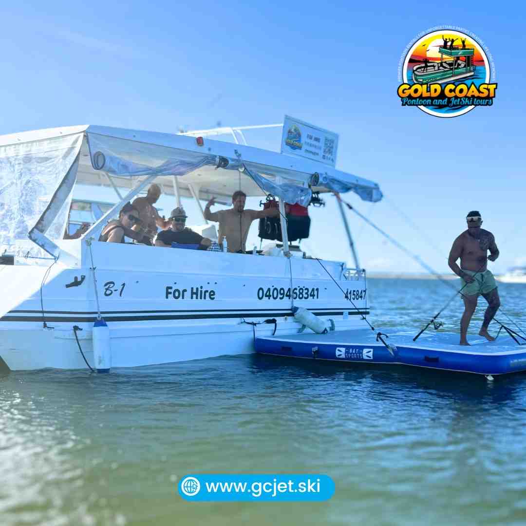 Pontoon boat with several people celebrating on deck, and a man with a fishing rod standing on an inflatable platform connected to the side - boat rental broadbeach