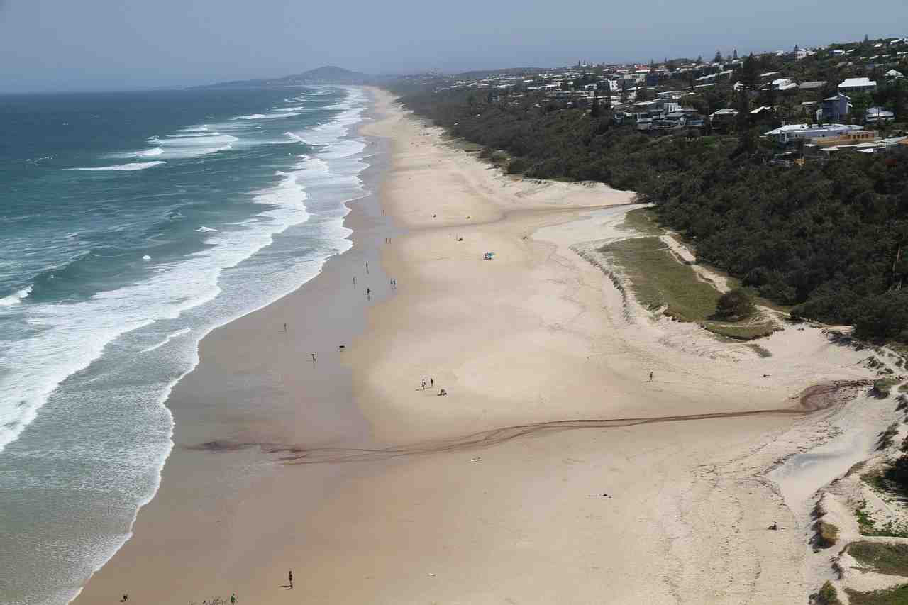 Aerial view of the long, sandy stretch of Gold Coast beach with white waves rolling in and dense coastal development - Gold Coast self drive
