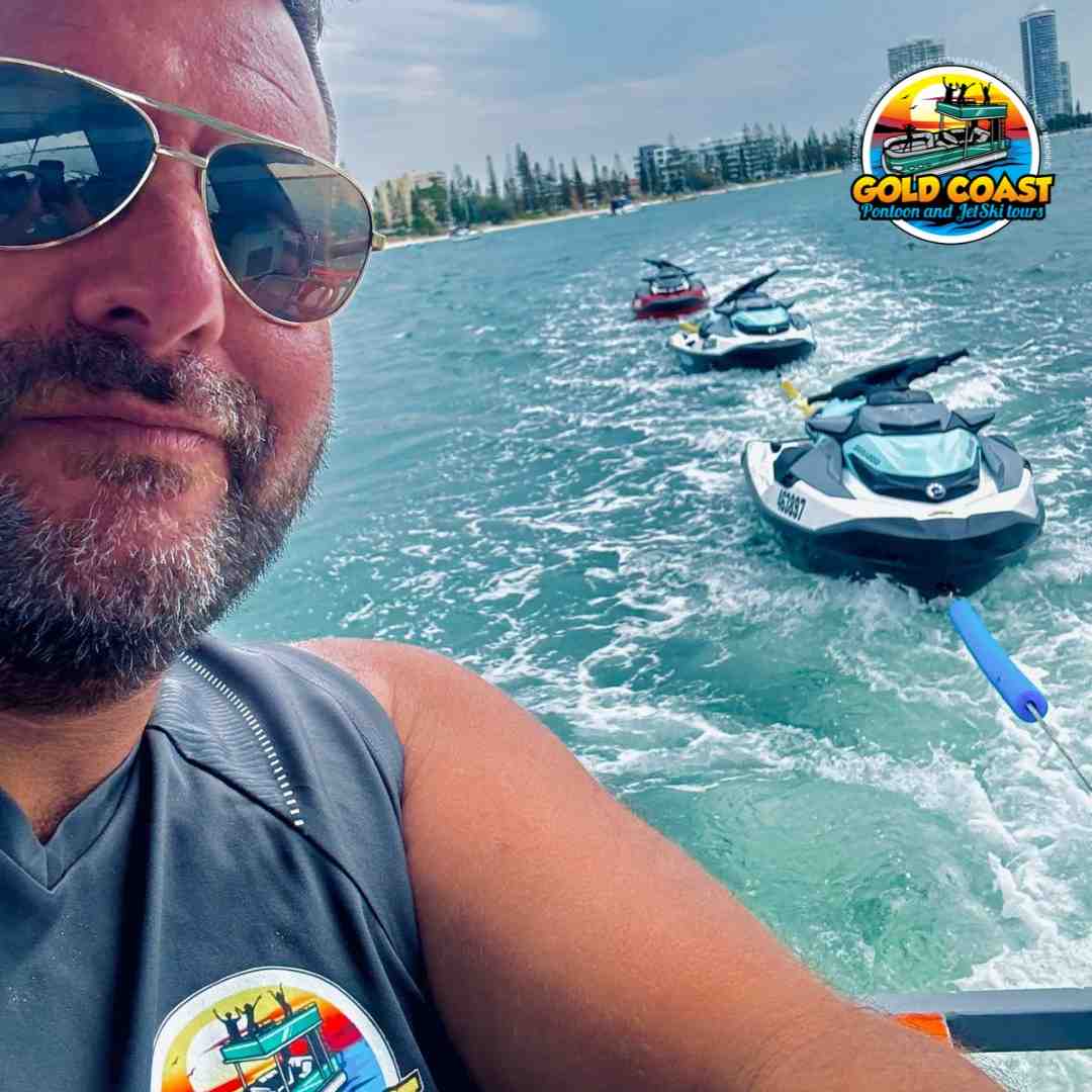 A man takes a selfie from his jet ski while towing a line of three other jet skis behind him on the water - water activities for groups