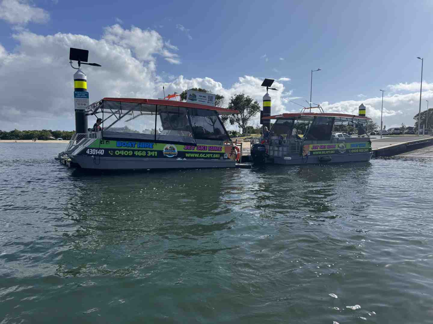 Two pontoon boats with covered tops are docked at a water ramp on a sunny day, ready for boat and jet ski hire - Surfers Paradise day trips