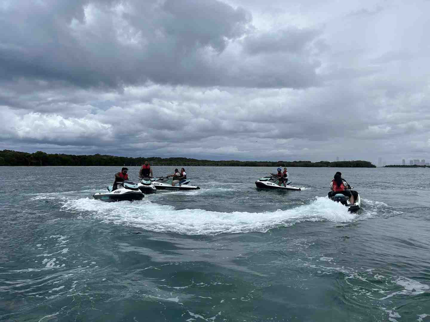Five pairs of people riding jet skis together on a water tour, creating wakes and turning under a dramatic, cloudy sky - Boat tours Gold Coast