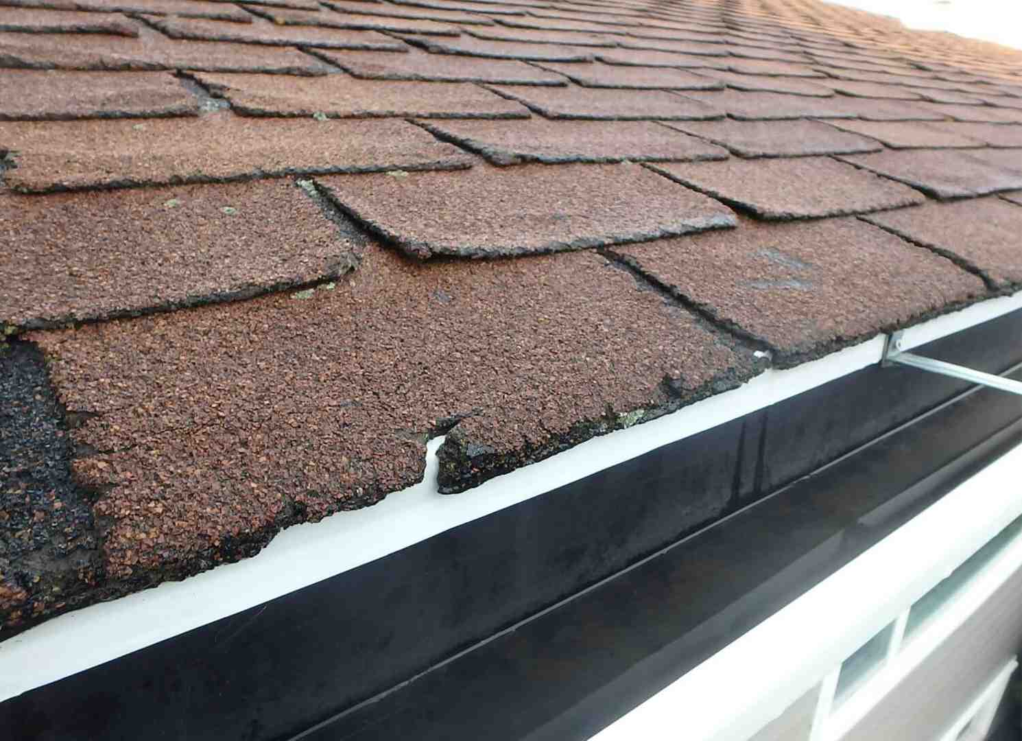 cracked and curling asphalt shingles on an old roof - Best roof replacement