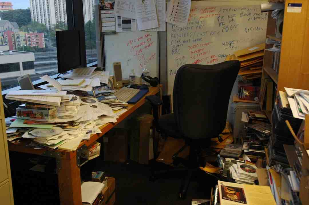 user-inserted Cluttered office workspace with piles of papers, manuals, CDs, and envelopes scattered across the desk and floor, highlighting inefficiency and disorganisation due to manual processes instead of CRM automation