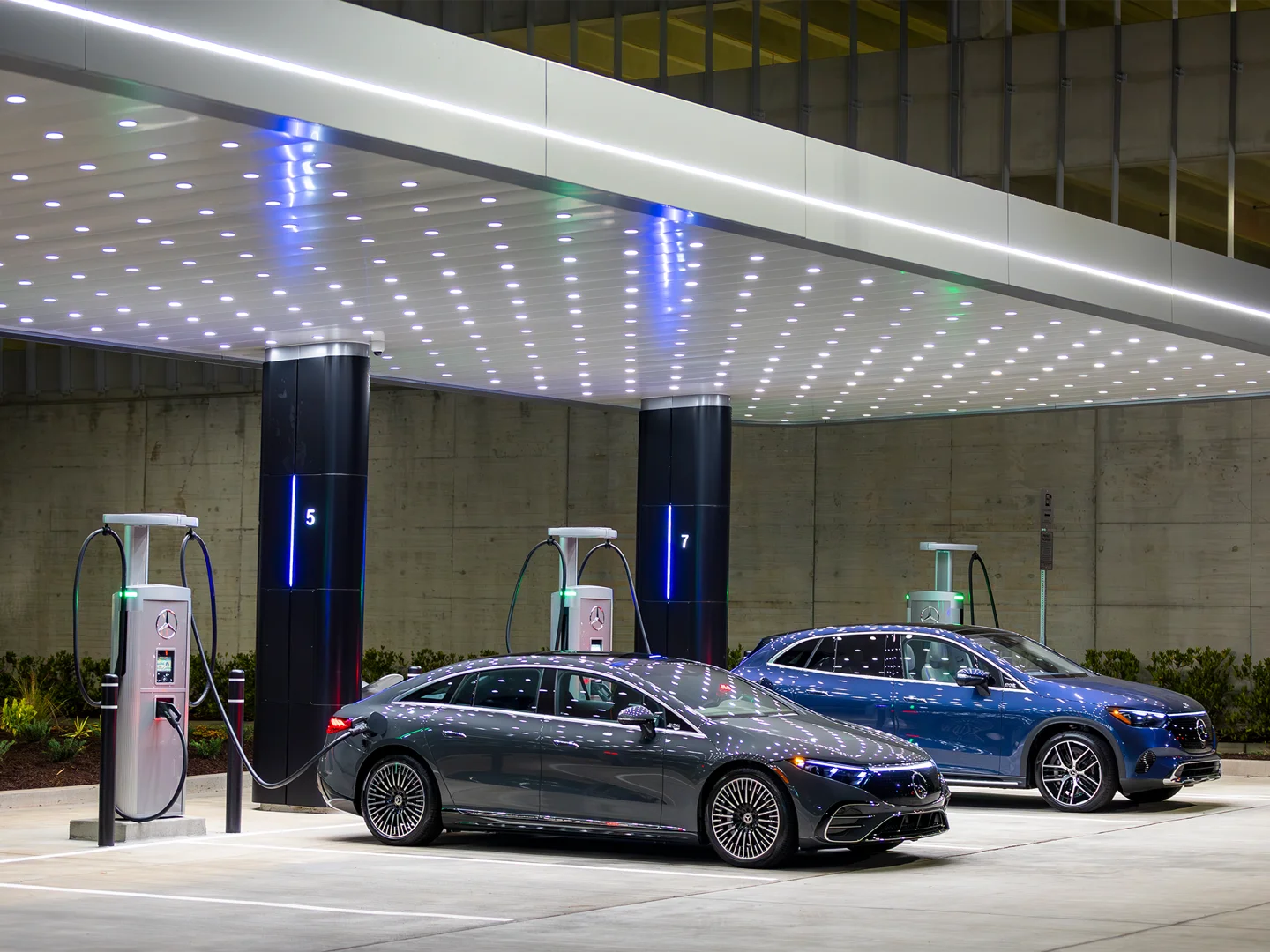 Two Mercedes-Benz electric vehicles charging at a modern, illuminated Mercedes-Benz fast-charging station.