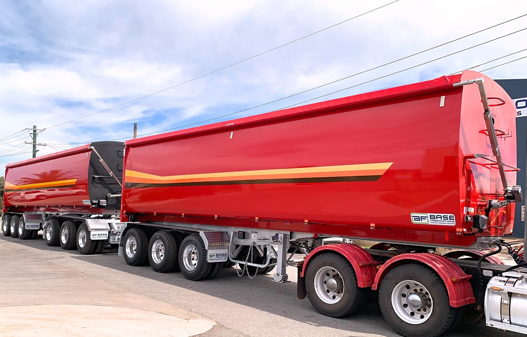 A dual-trailer truck featuring high quality load tarps in a sleek red finish, secured with a roll-over tarp system.