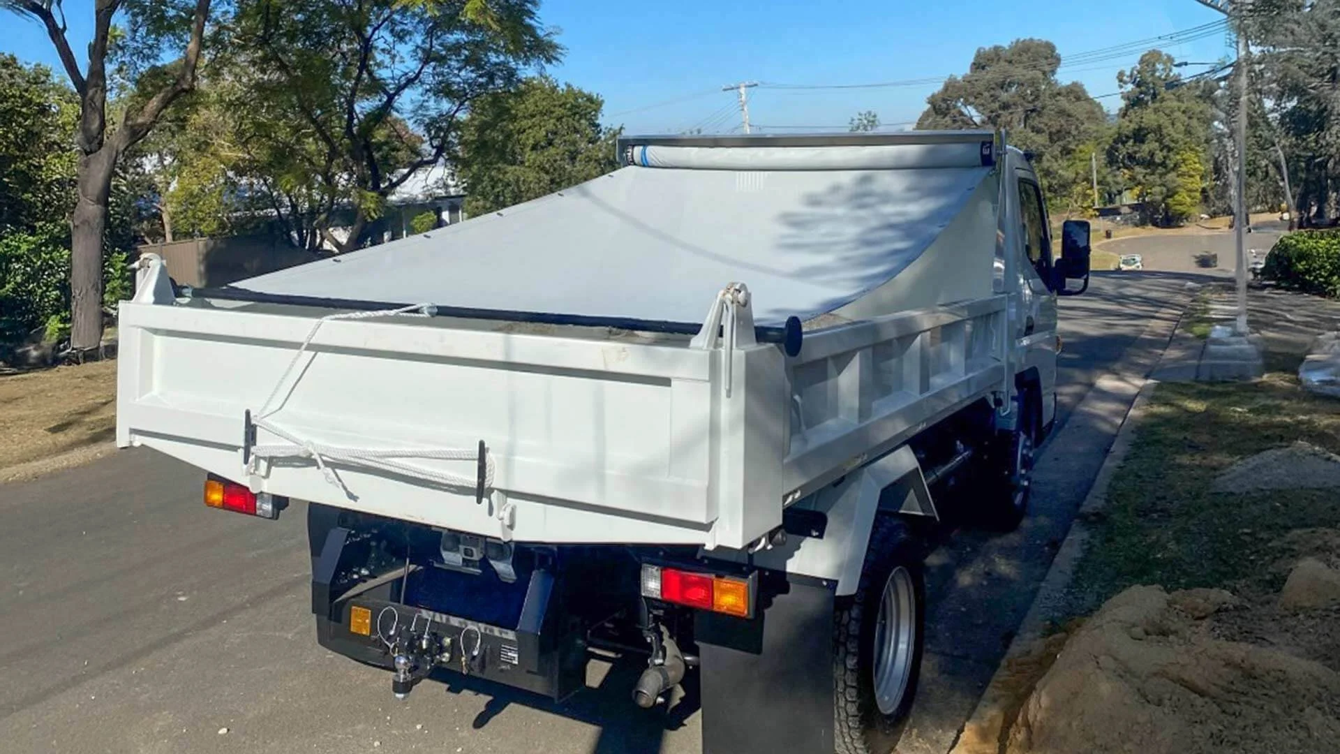A white dump truck with a pull-out retractable tarp system covering the load bed. A white dump truck with a pull-out retractable tarp system covering the load bed.
