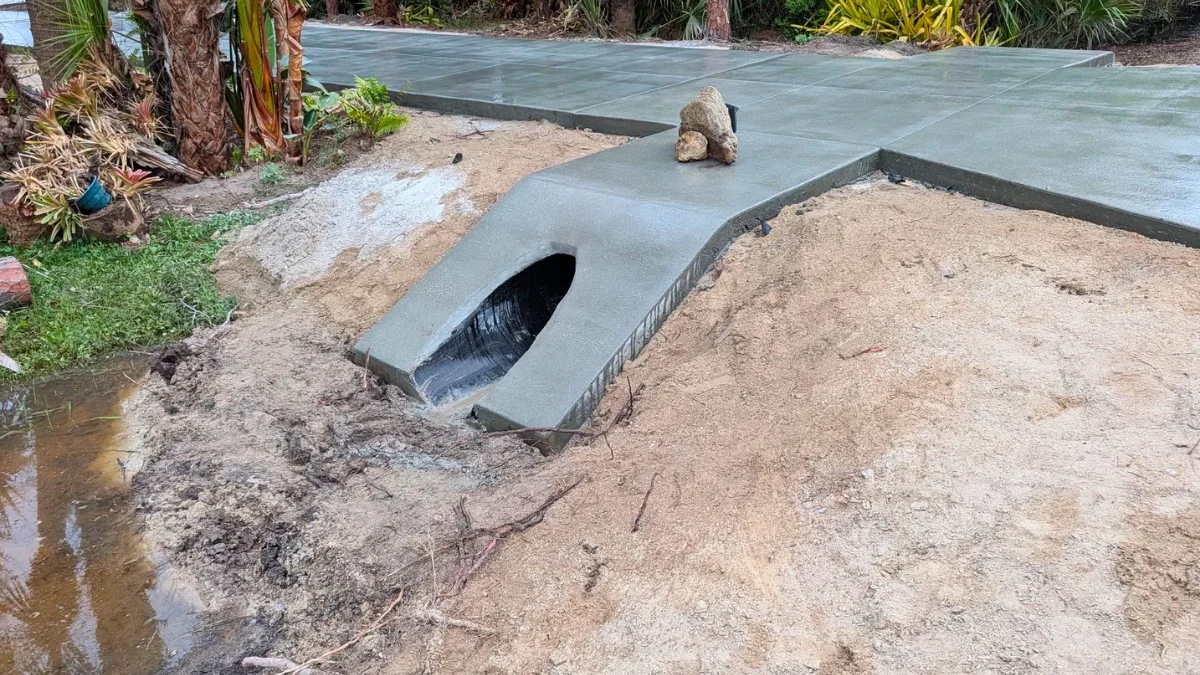 drainage pipe under driveway with concrete culvert end and sandy soil around a finished driveway
