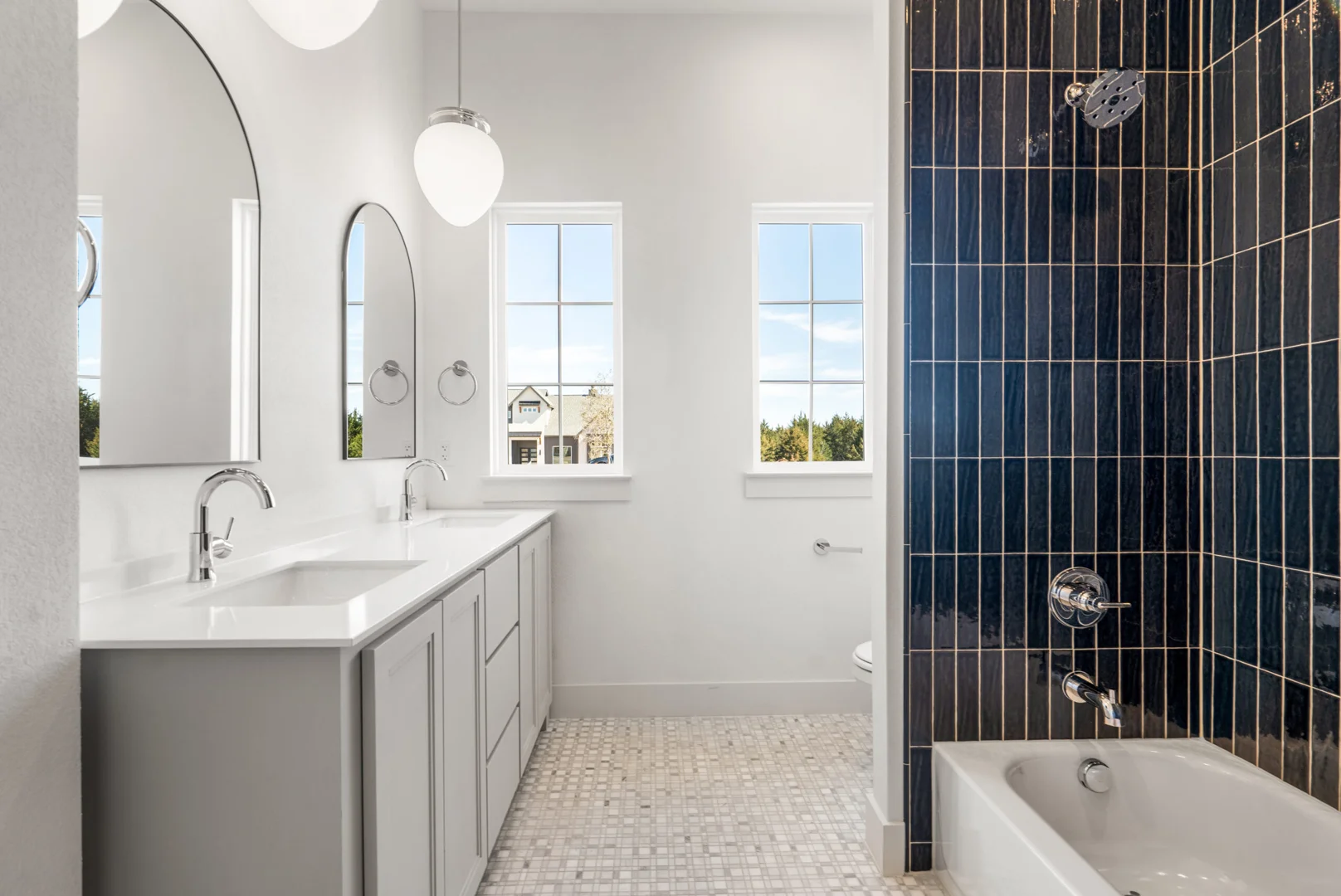 Bright custom bathroom with white vanity cabinetry, arched mirrors, and a deep navy tiled shower wall