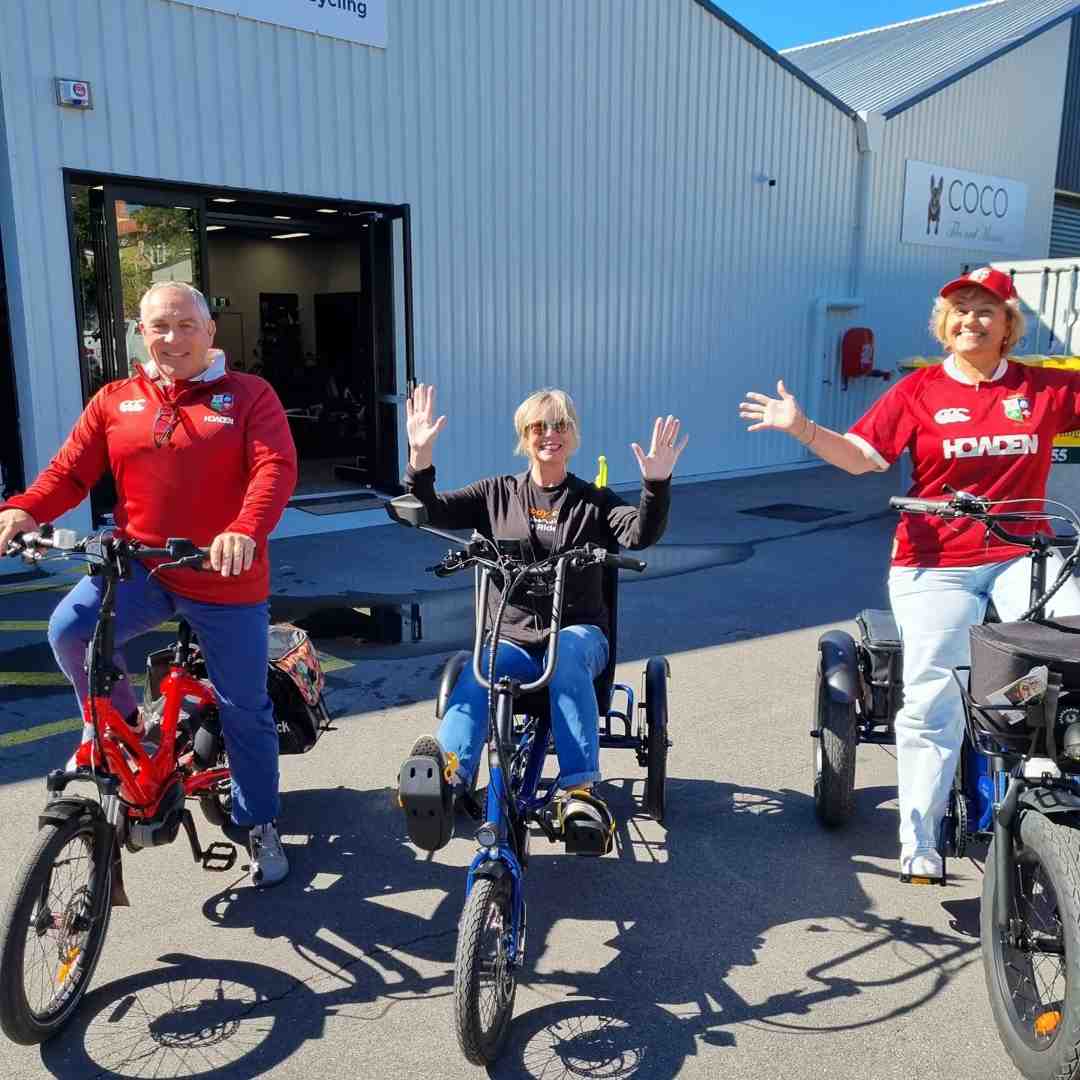 Three adults smiling and posing on electric bikes and trikes outside our Brisbane store.
