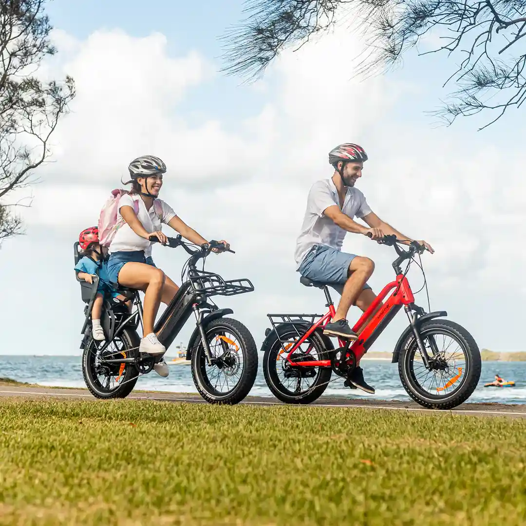 Family riding Velectrix electric bikes along a coastal path, with a child seat attached to one bike for carrying kids.