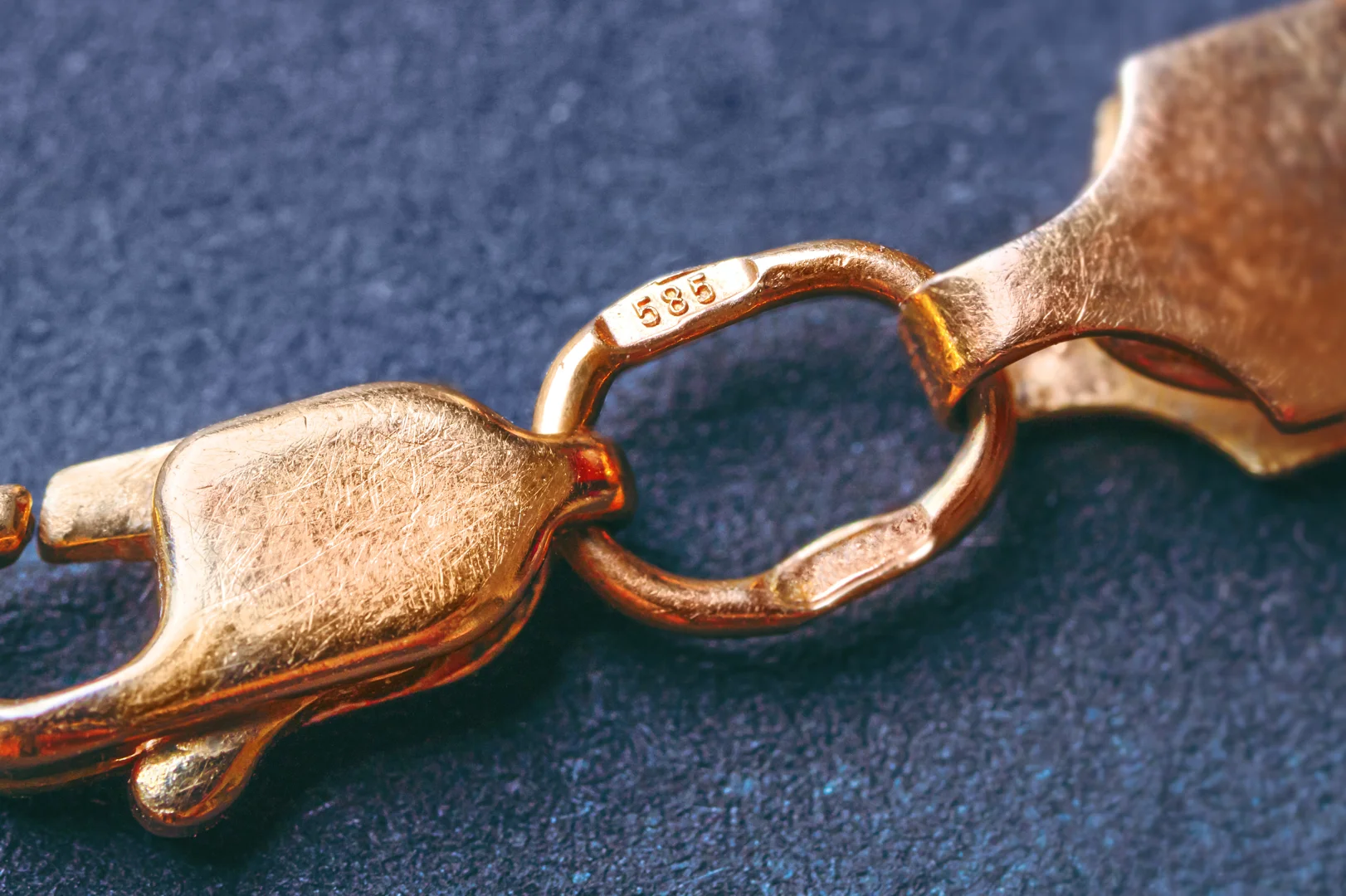 A gold clasp with a stamp of "585" to represent 14-karat gold on a dark, slightly textured blue fabric background.