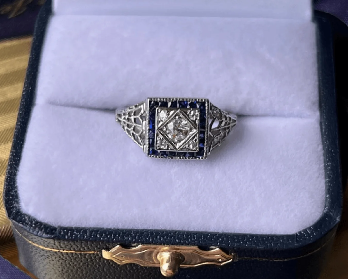 An antique Art Deco diamond and blue sapphire filigree ring in a luxury Nelson Coleman Jewelers ring box.