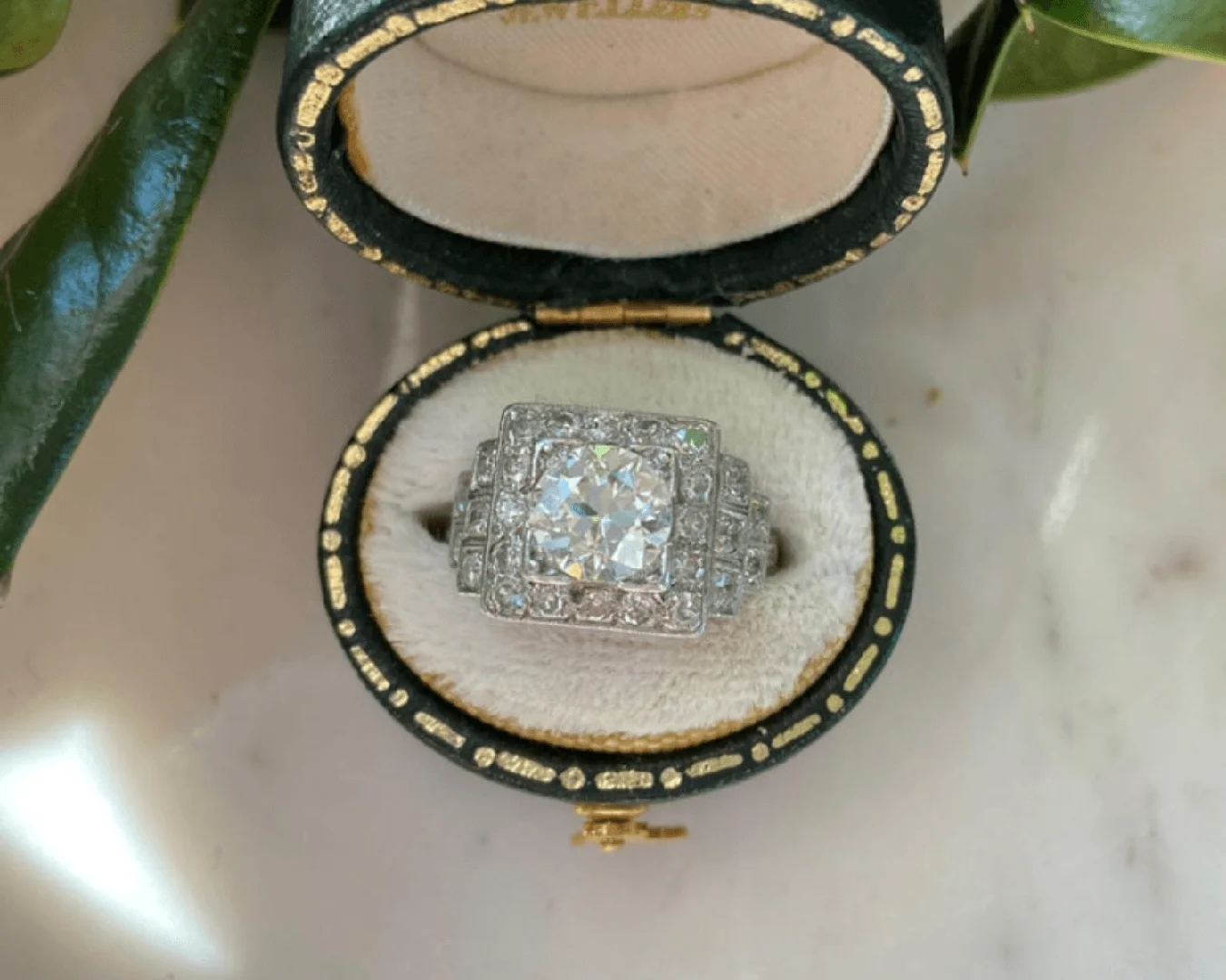 An antique Art Deco old European-cut diamond engagement ring in a small oval-shaped ring box.