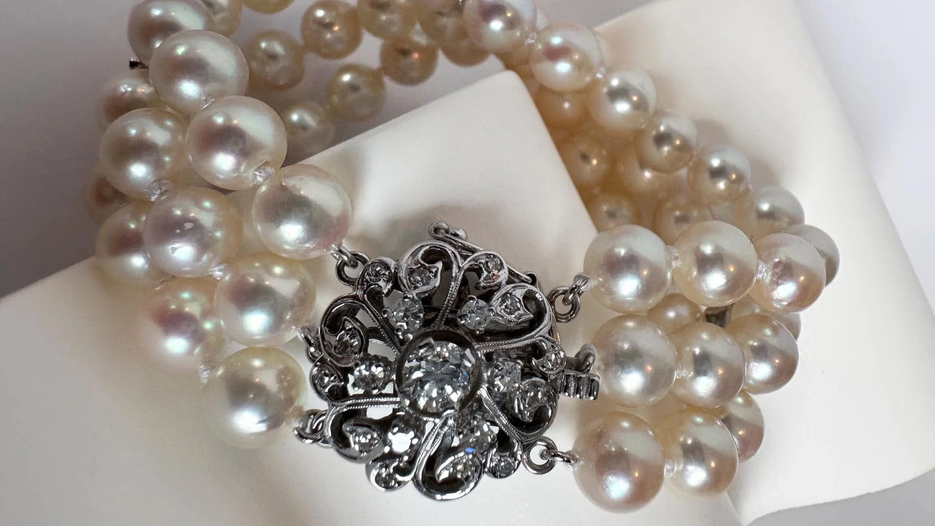 An antique multi-strand pearl bracelet with a diamond-accented clasp on a white background.