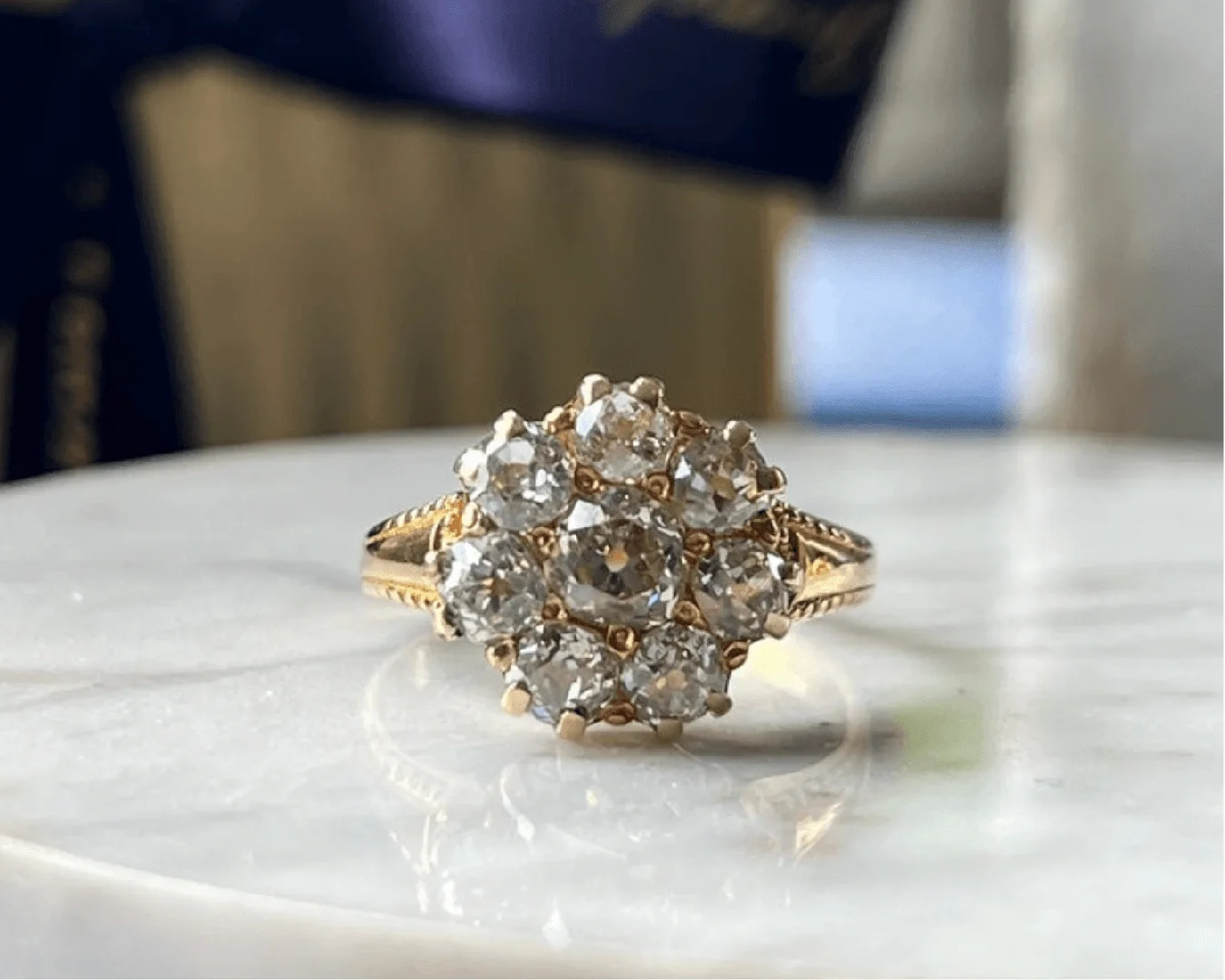 An antique Victorian yellow gold diamond cluster ring on a reflective white marble surface.