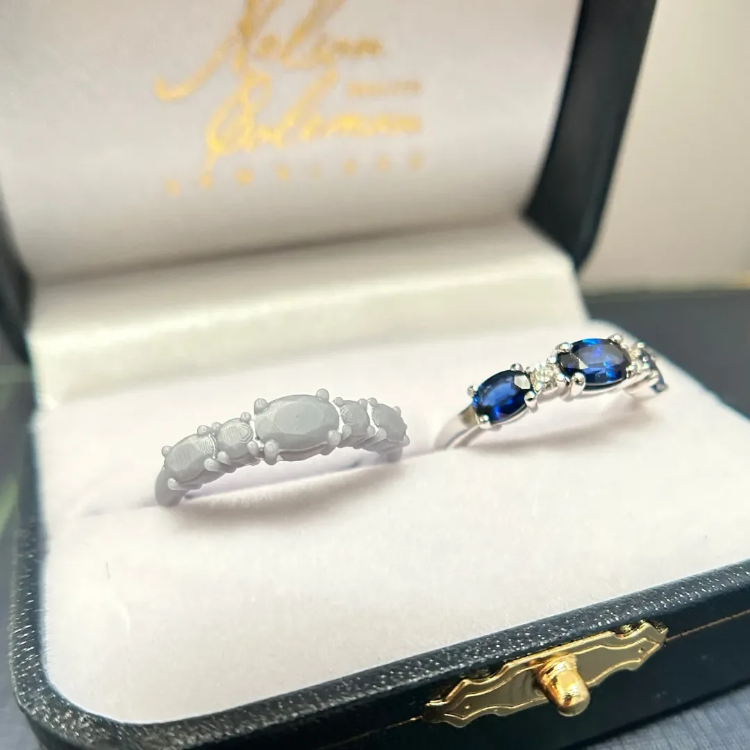 A wax model and finished product of a custom-designed white gold oval blue sapphire and diamond anniversary band in a Nelson Coleman Jewelers luxury jewelry box.