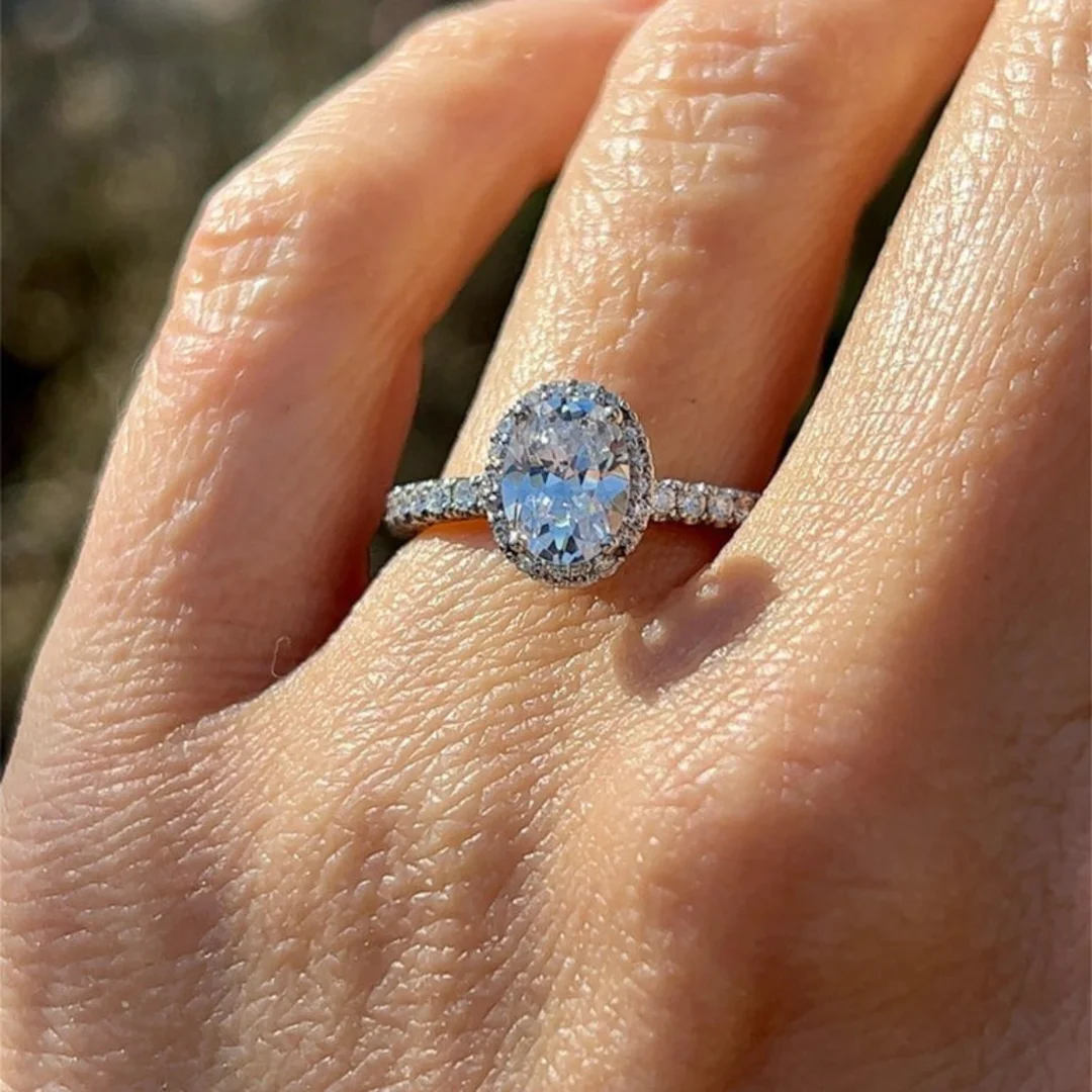 A close-up image of an estate Tacori oval diamond halo engagement ring on a woman's left ring finger.