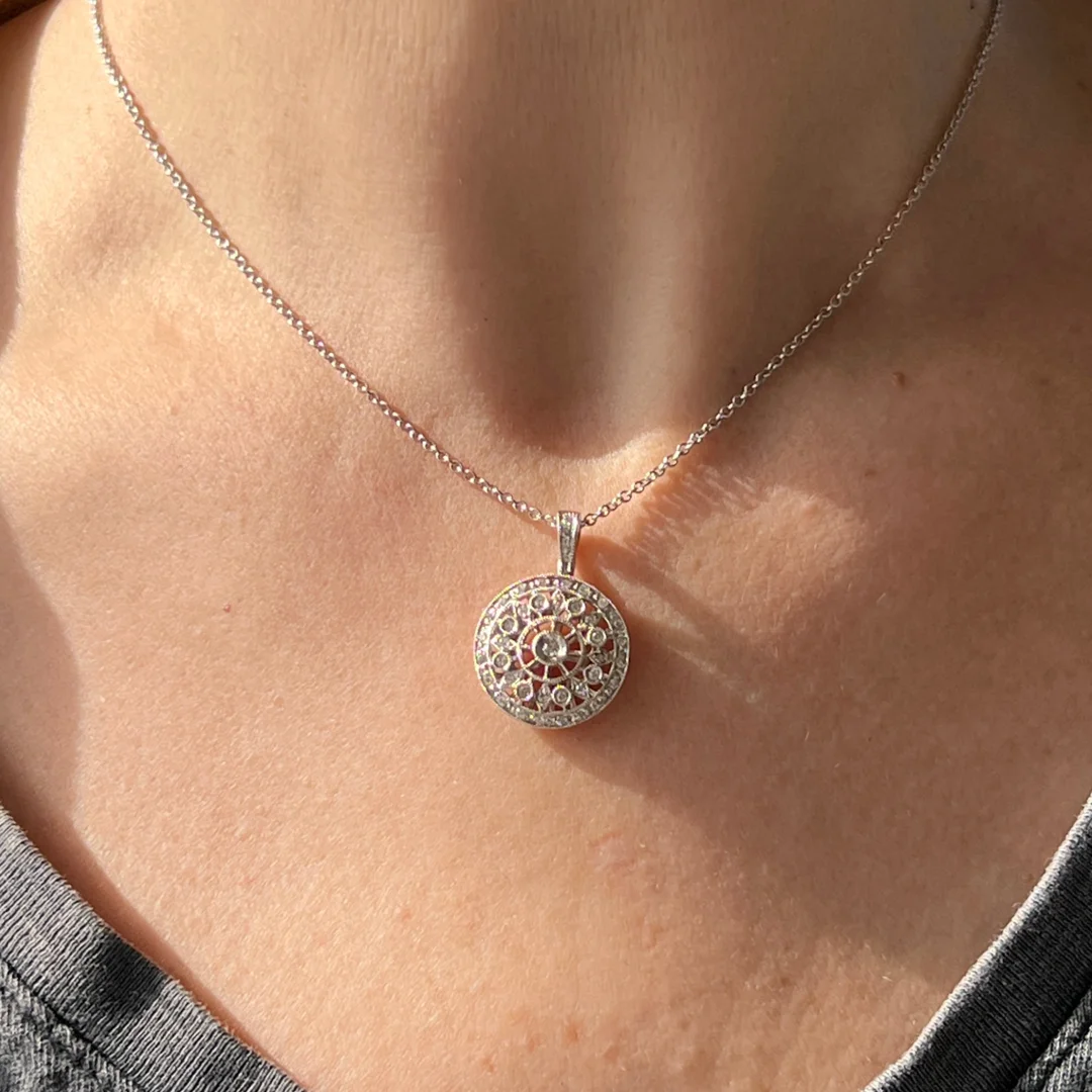 A close-up image of a woman wearing an intricate diamond filigree, cluster, and halo pendant necklace in a two-tone gold setting on a white gold chain.