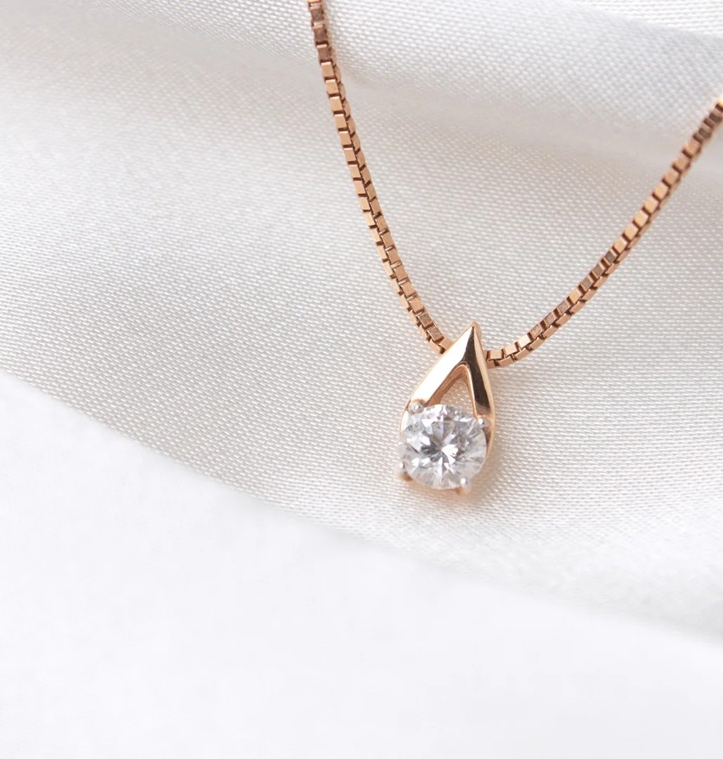 A close-up of a diamond solitaire pendant necklace in a yellow gold setting in soft white fabric.