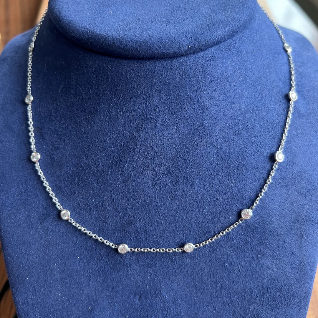 A white gold diamond station necklace on a blue velvet display.