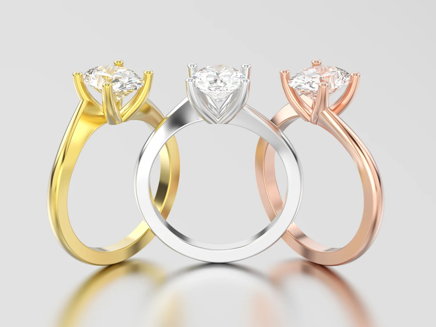 Three diamond solitaire engagement rings in different metal colors, including yellow gold, white gold, and rose gold, on an isolated reflective light grey surface.