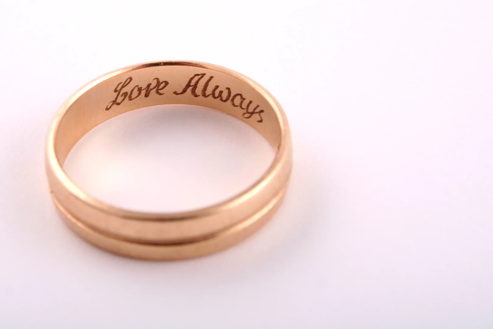 A gold wedding band with the words "Love Always" in script engraved on the inside of the band.