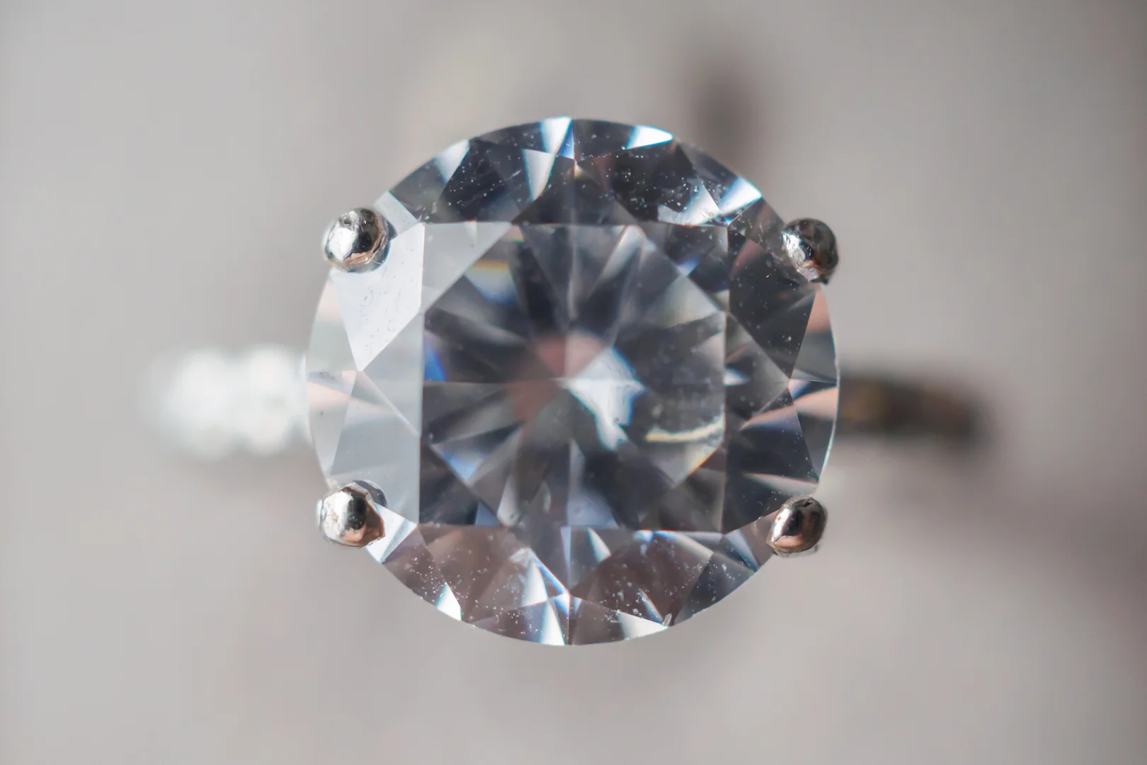 A close-up image of a white gold four-prong round brilliant-cut diamond solitaire engagement ring. A close-up image of a white gold four-prong round brilliant-cut diamond solitaire engagement ring.
