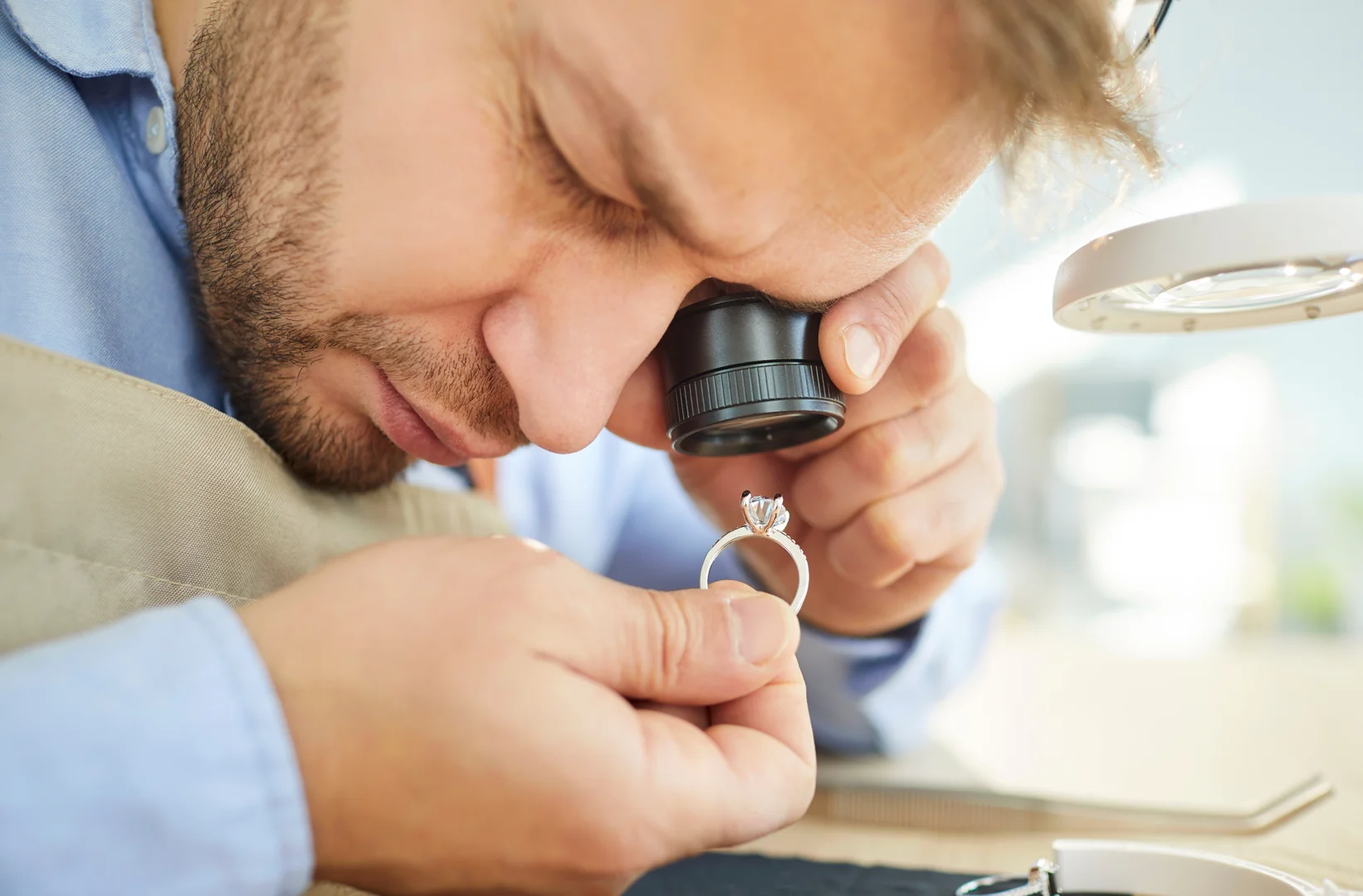A jeweler using a jeweler's loupe to inspect a diamond ring up close.