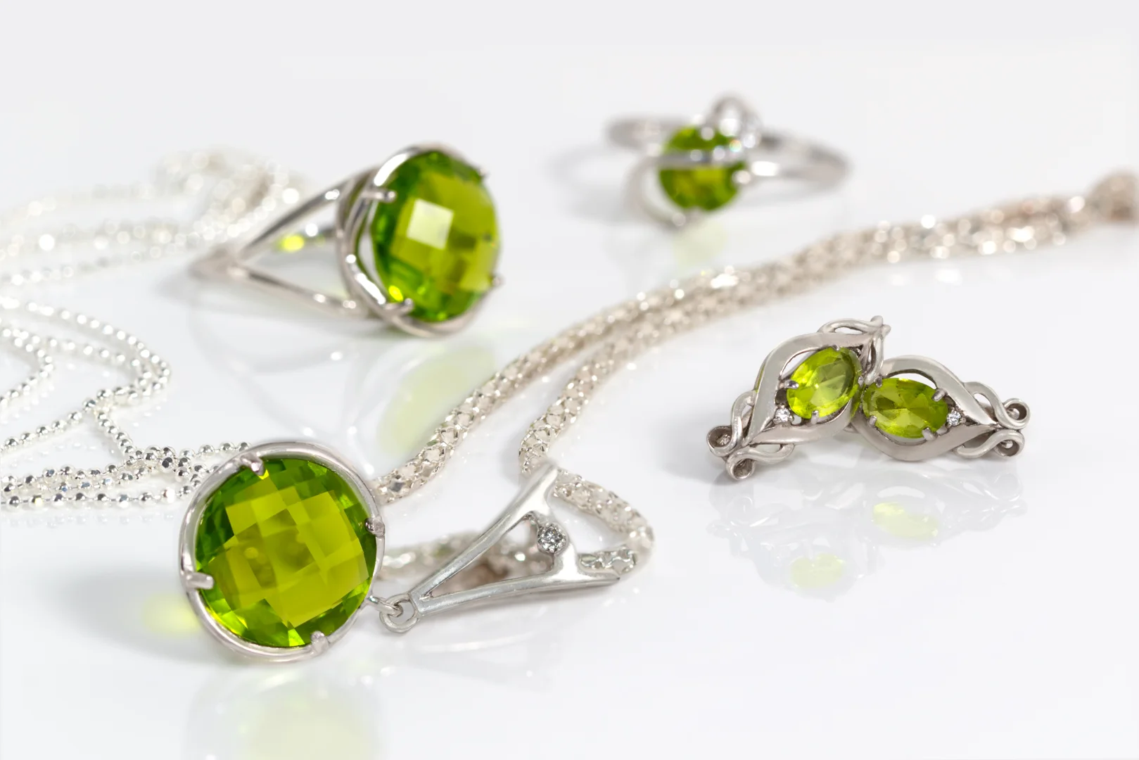 A collection of fine peridot jewelry on a reflective white surface