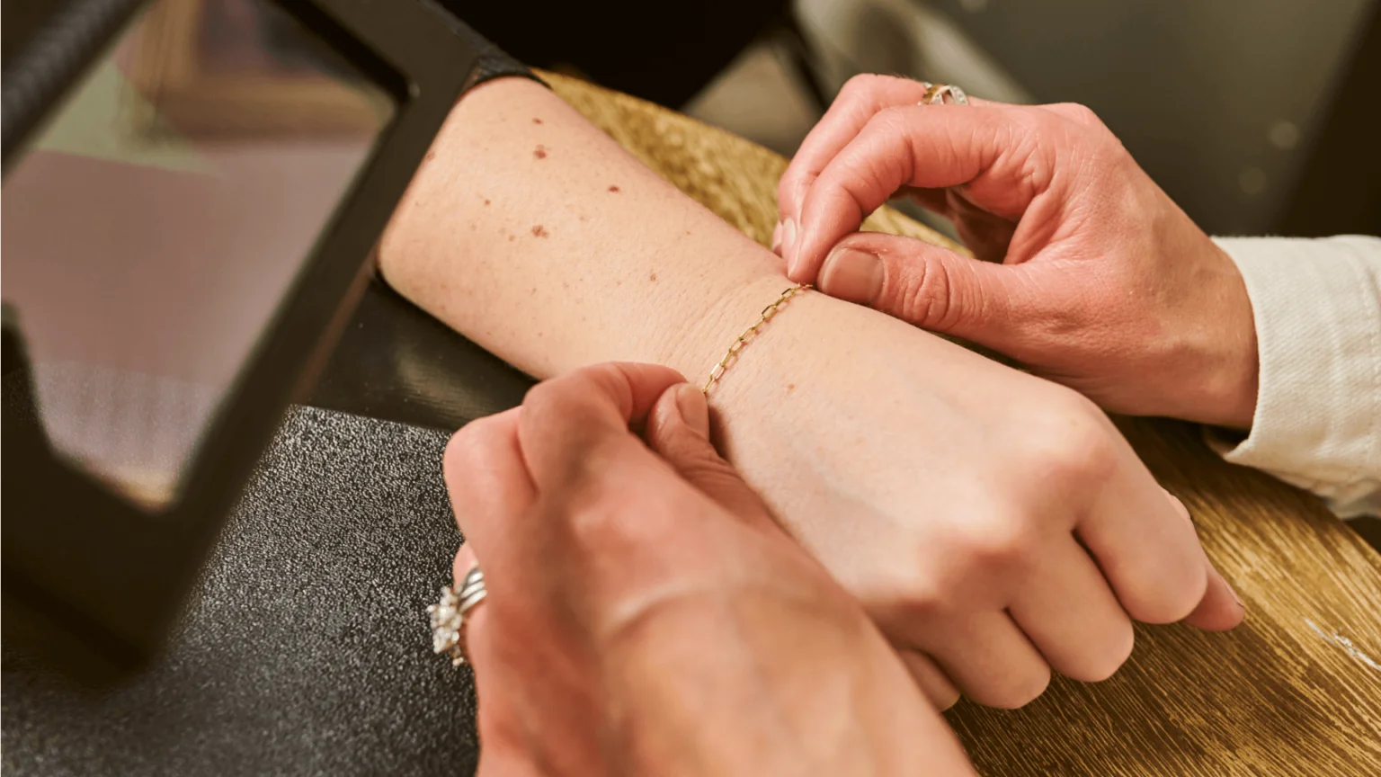 A jeweler gently adjusts a 14 karat yellow gold permanent jewelry chain bracelets on a woman's wrist.