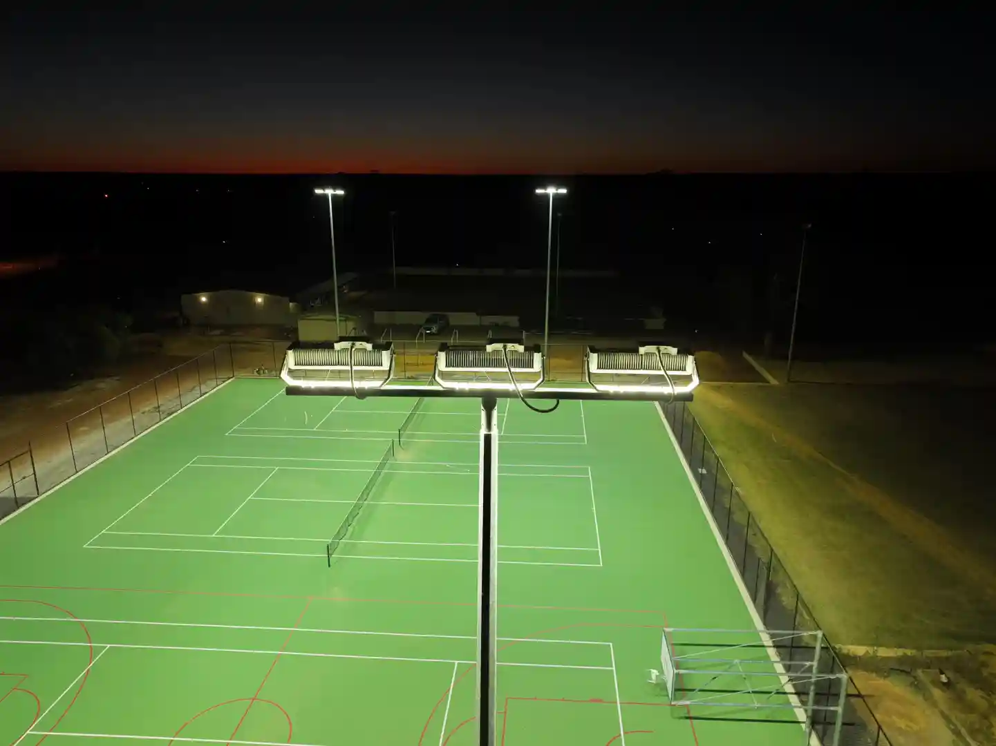 A community sports field at night, brilliantly illuminated by Vizona's LED sports lighting, showing active play - smart outdoor lighting