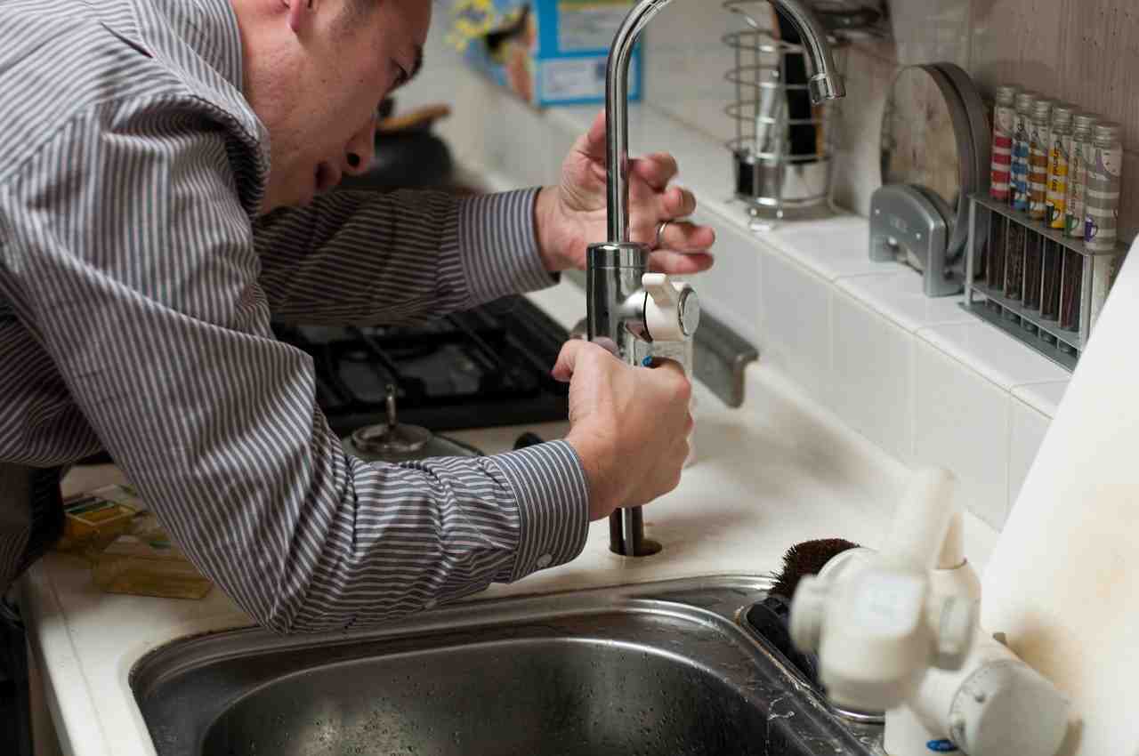Photo of a plumber servicing a residential bathroom sink, illustrating common household drain issues - cost to unclog drain