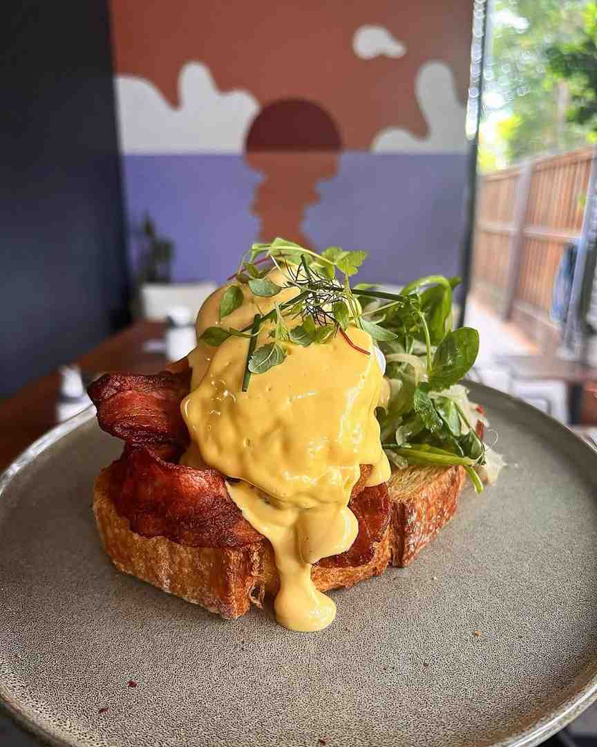 Bacon Benedict with hollandaise sauce pouring over poached eggs - 5 Brunch Dishes You Need to Try at Flinders Lane Café