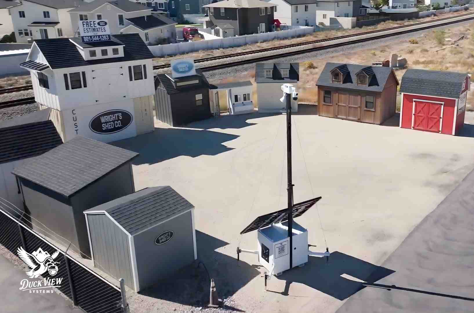 Mobile Surveillance Trailer Monitoring Outdoor Storage Yard Aerial view of a mobile surveillance trailer with solar panels monitoring a shed display yard and surrounding buildings.