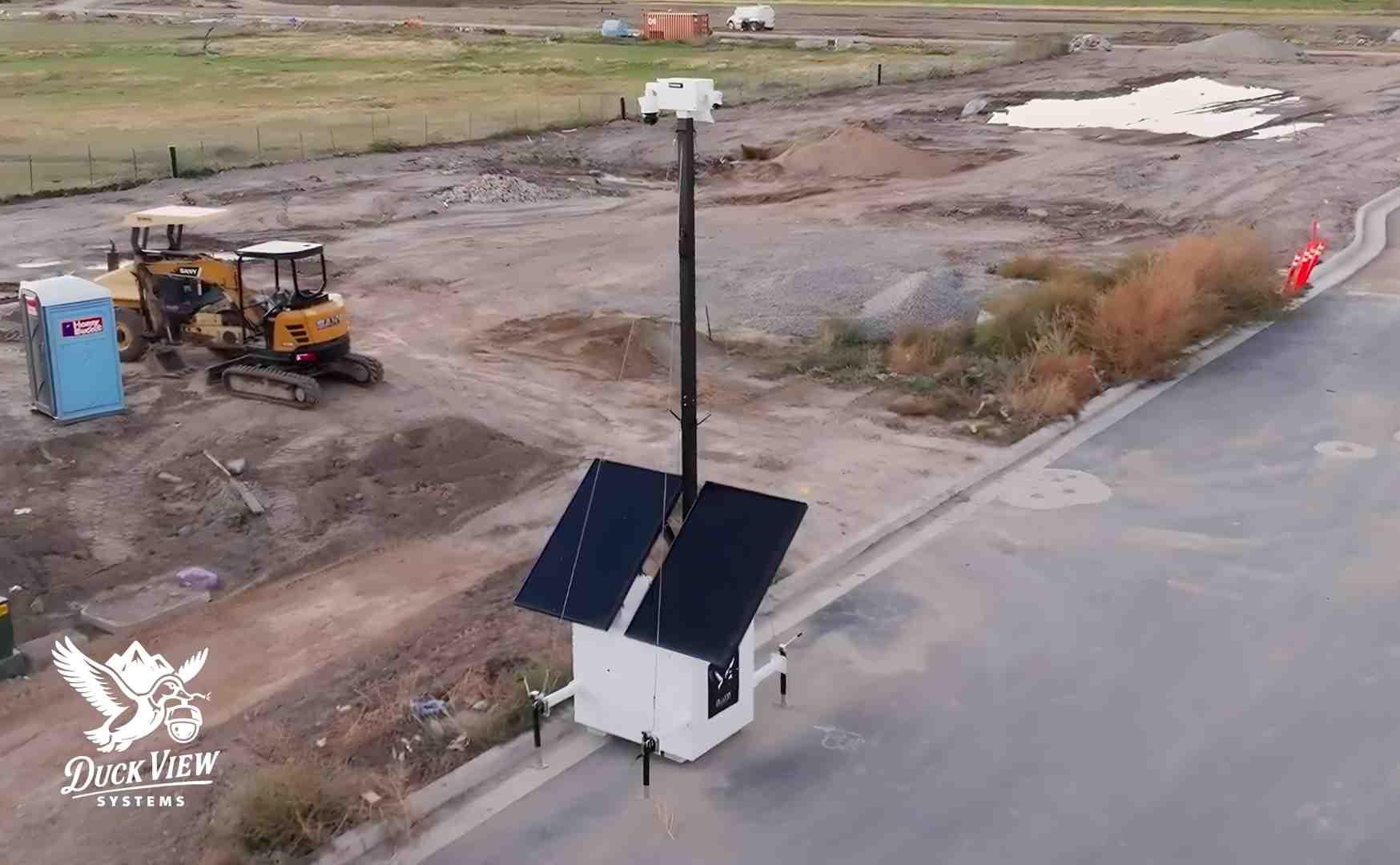 Mobile Surveillance Trailer Monitoring Active Construction Site Duck View Systems mobile surveillance trailer with solar panels providing elevated, real-time monitoring across an active construction site with heavy equipment.