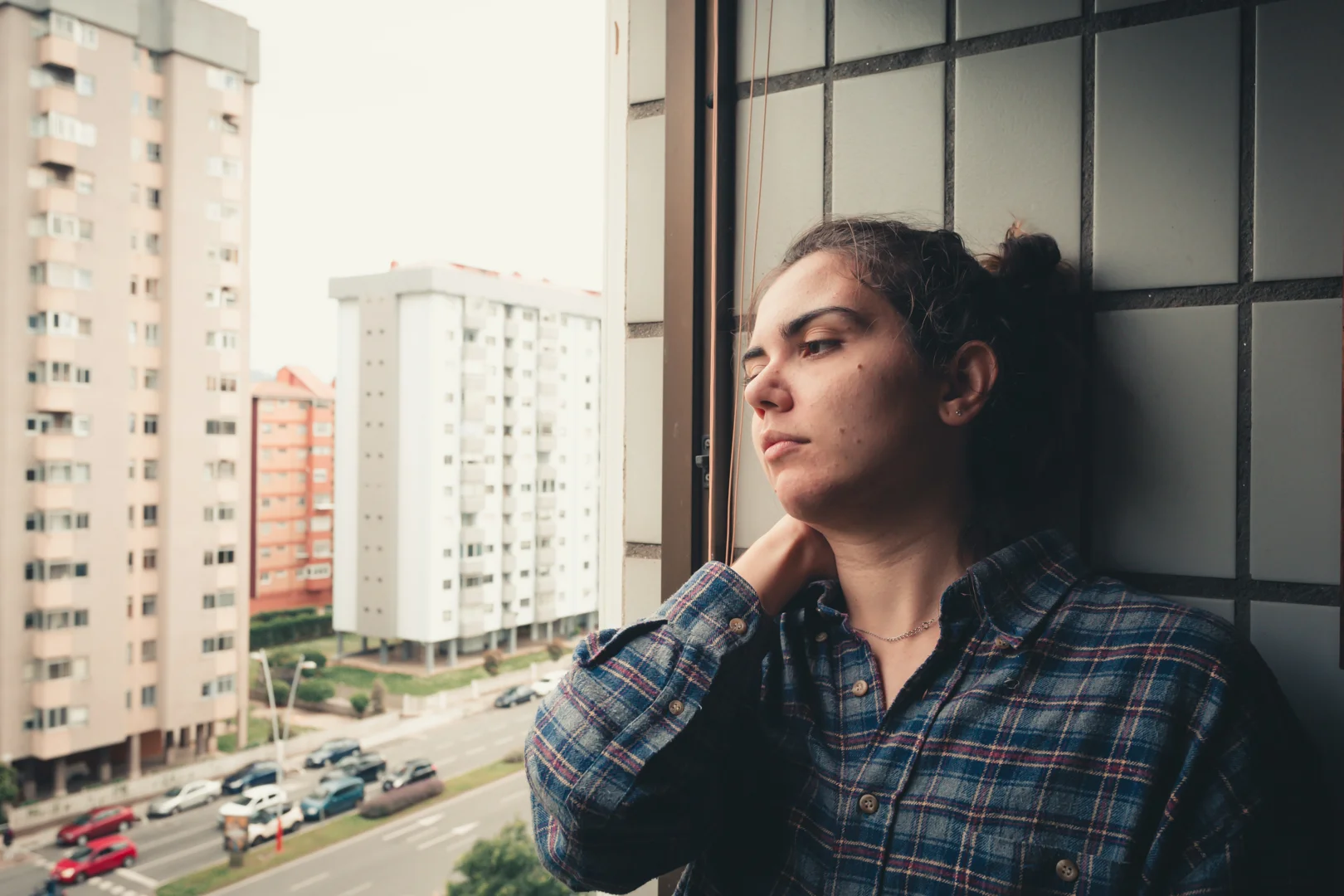 Person looking thoughtfully out of a window with a view of a Barcelona street - Personalized mental health care