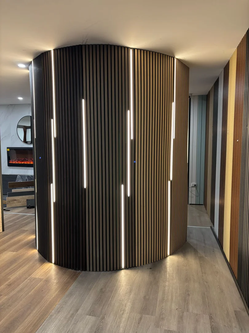 A curved interior wall featuring vertical wood slat acoustic panels with integrated linear LED lighting for a modern look.